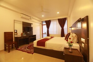 A hotel room with a bed, a desk, a chair, a TV, and a window with curtains. - Hotel Mountain Hues Thekkady (Udumbanchola)