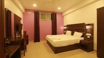 Habitación de hotel con cama, mesita de noche, escritorio, silla, cortinas y ventilador de techo.