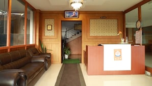 A reception area with a wooden reception desk, a brown leather sofa, a staircase, and a chandelier. - Hotel Mountain Hues Thekkady (Udumbanchola)