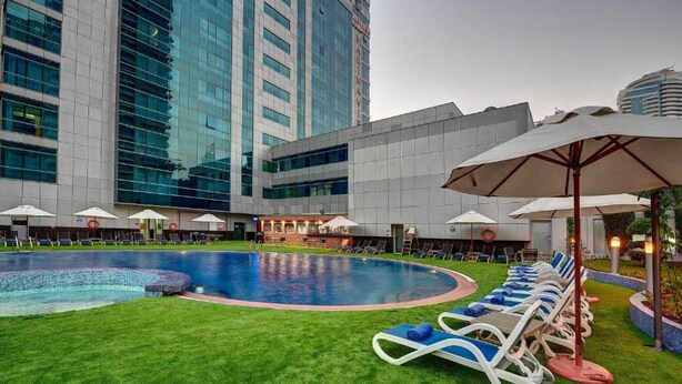 A hotel pool area with a large pool, lounge chairs, umbrellas, and a modern building in the background. - Belvilla Marina View Suites, Dubai Marina (Dubai)
