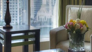 A room with a table, a lamp, a vase with flowers, a chair, and a view of a cityscape through large windows. - Belvilla Marina View Suites, Dubai Marina (Dubai)