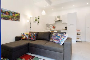 A modern living room with a sectional sofa, a painting on the wall, and a kitchen in the background.