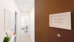 A hallway with a framed sign on the wall, a potted plant, and a door with a lock.