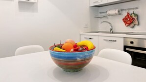 A modern kitchen with white cabinetry, a stainless steel sink, and a bowl of fruit on the counter.