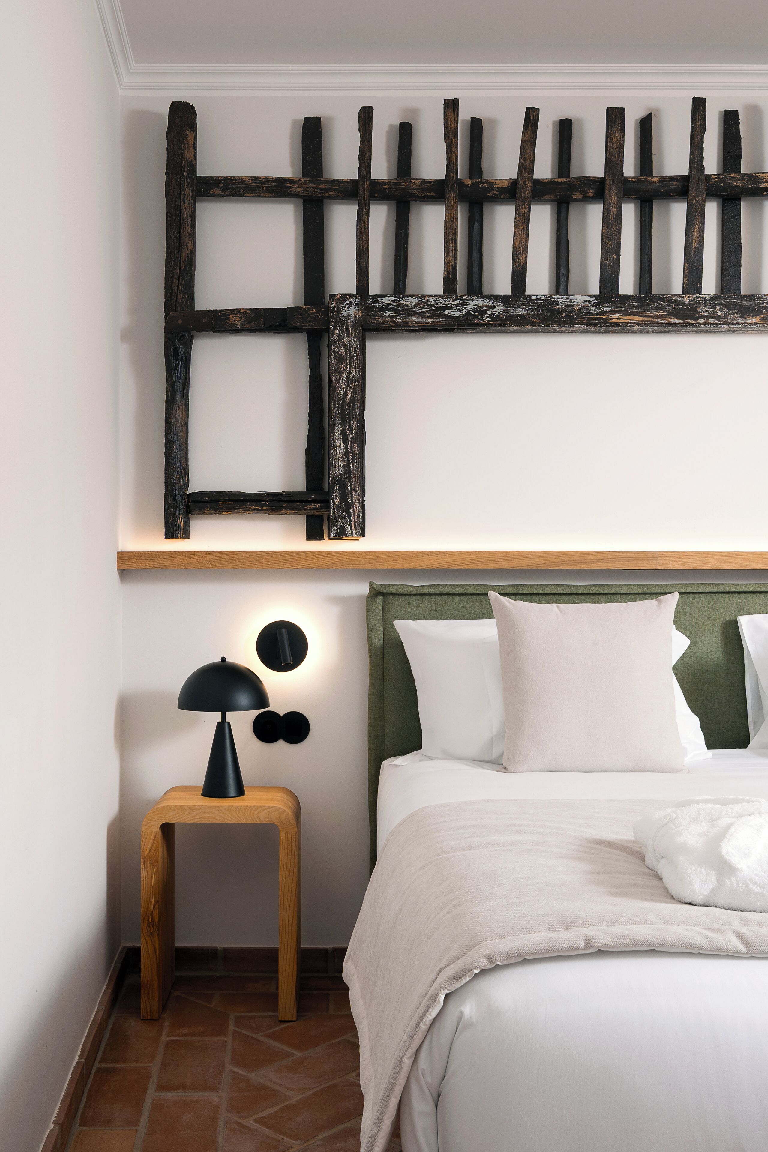 A bedroom with a wooden headboard, a bedside table with a lamp, and a bed with white bedding.