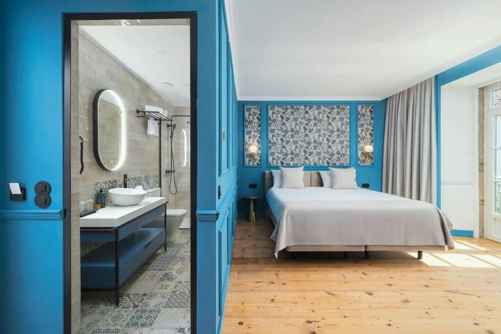 A modern bedroom with a large bed, a bathroom with a sink and mirror, and patterned tiles.