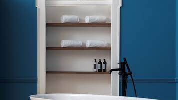 A freestanding bathtub in a bathroom with a built-in shelf unit above it, holding towels and toiletries.