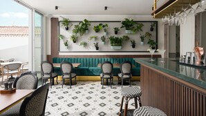 A modern bar area with a green cushioned bench, patterned chairs, and a tiled floor. - Água Hotels Lagos Bay (Lagos)