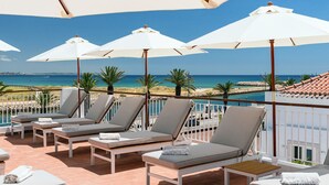 A balcony with sun loungers and umbrellas overlooking a beach. - Água Hotels Lagos Bay (Lagos)