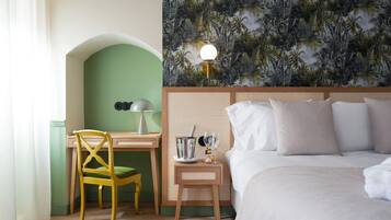 Une chambre d’hôtel comprenant un lit, un bureau avec une chaise, une table de chevet avec une lampe et un mur recouvert d’un papier peint aux motifs tropicaux.