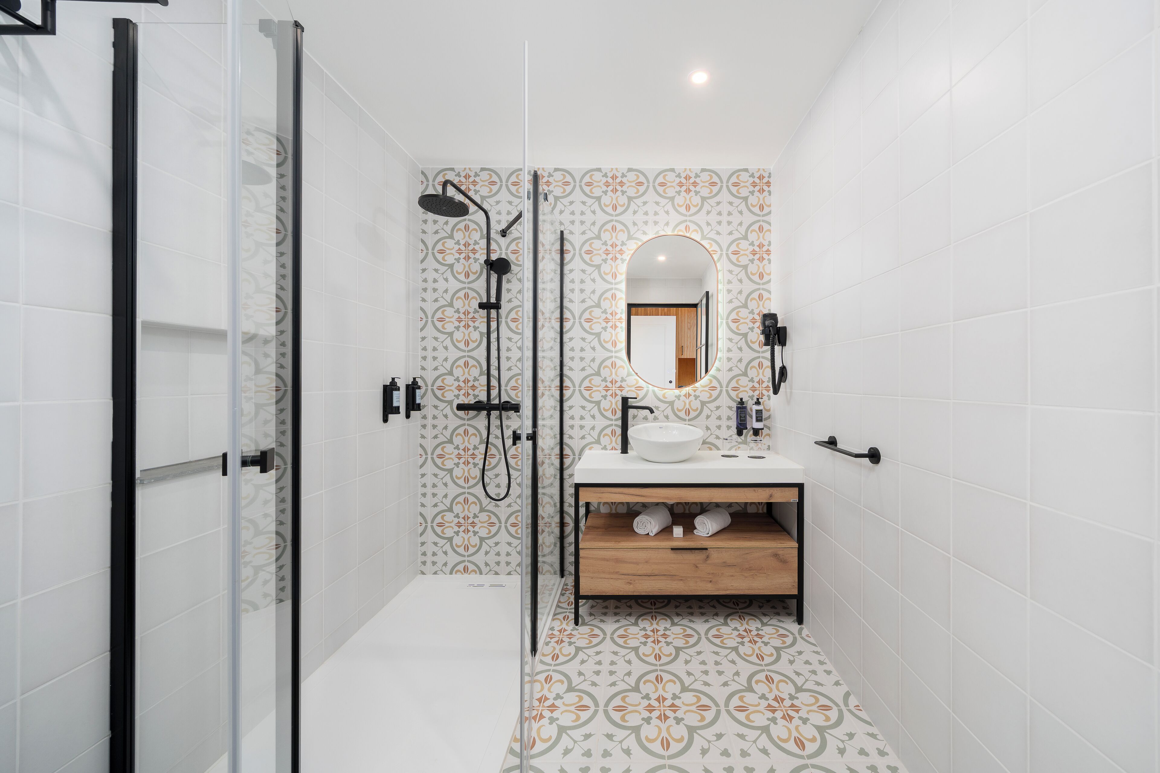 A modern bathroom with a glass shower enclosure, a sink with a mirror, and patterned floor tiles.