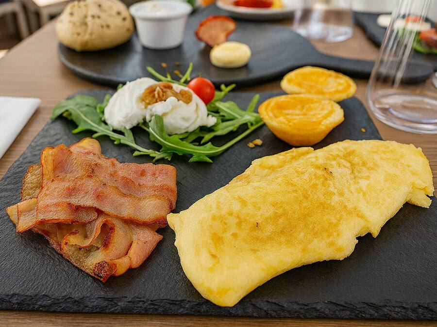 A breakfast plate with bacon, an omelette, and a salad on a slate board.