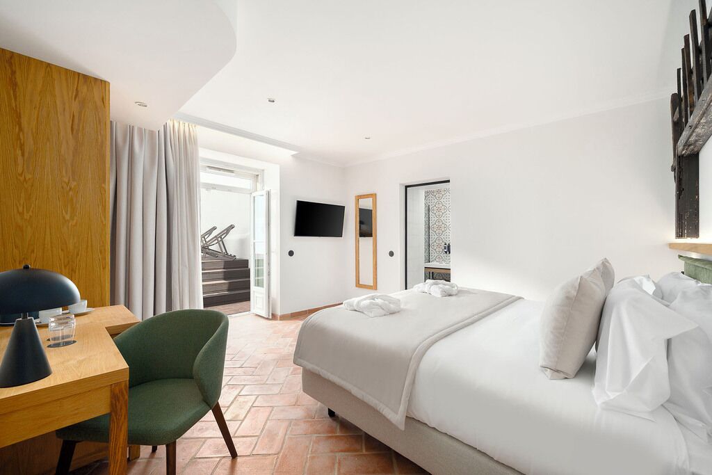 A hotel room with a bed, a desk, a chair, a TV, and a view of the outside.
