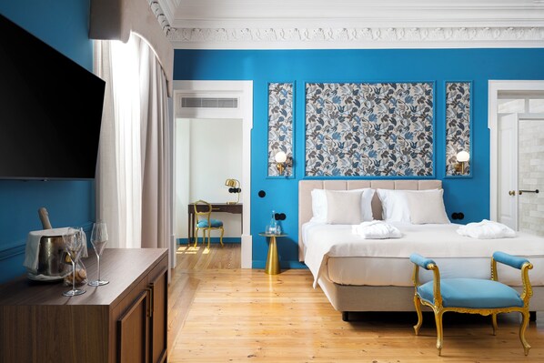 A bedroom with a blue wall, a bed with white bedding, a blue chair, a wooden dresser, and a flat-screen TV.