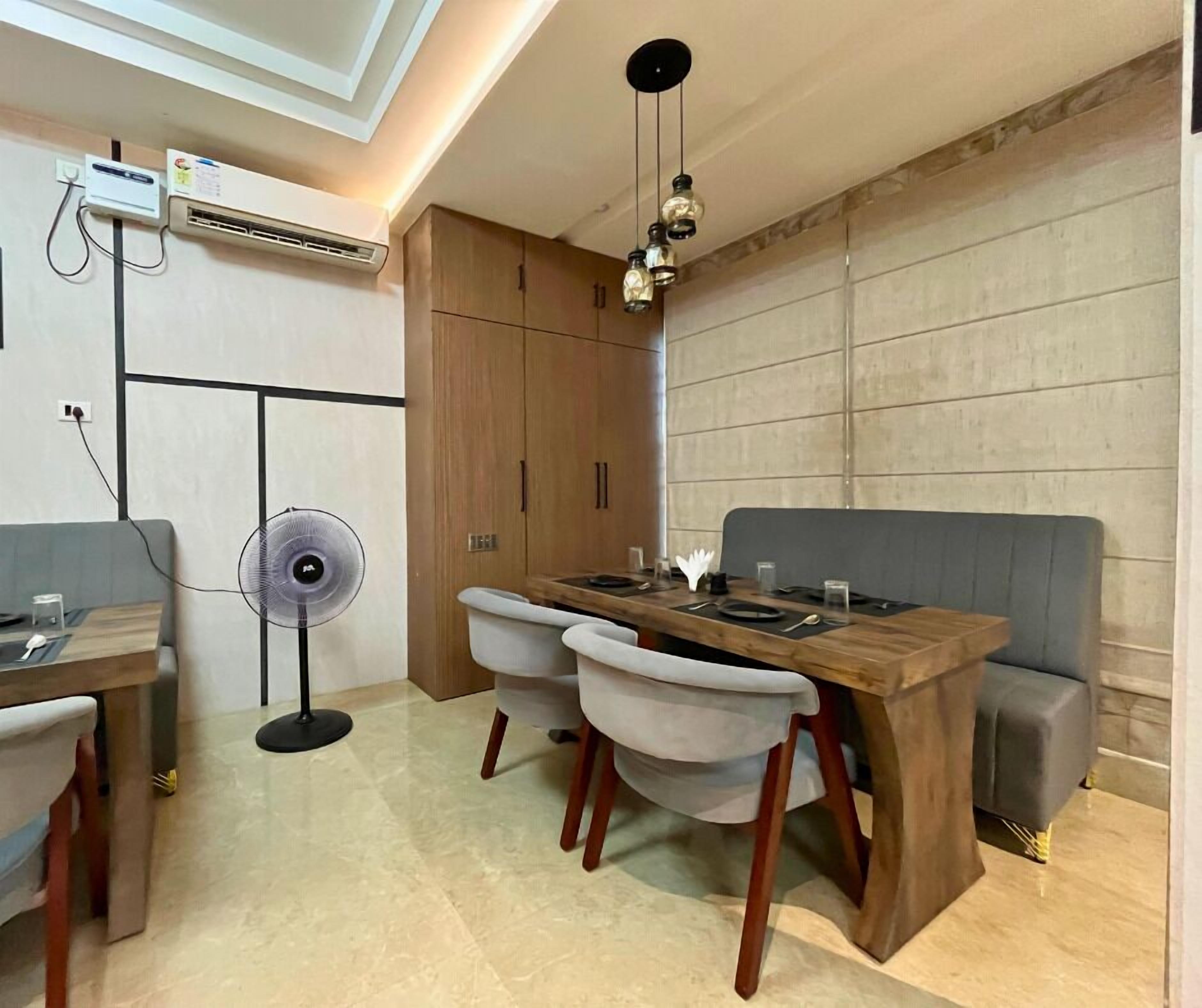 A dining area with a wooden table, two chairs, a bench, and a standing fan.