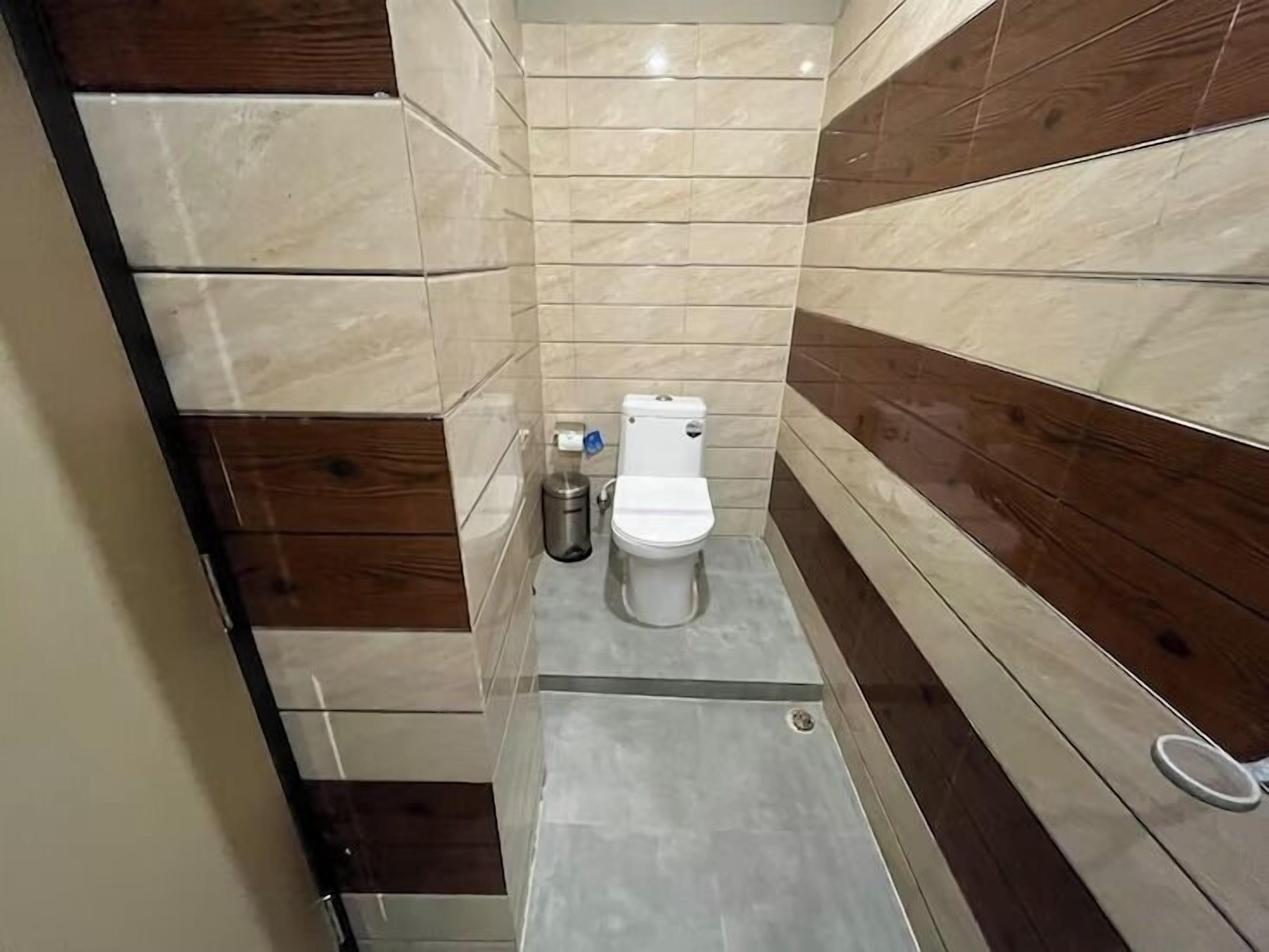 A small, narrow bathroom with a toilet, a trash bin, and a shower area.
