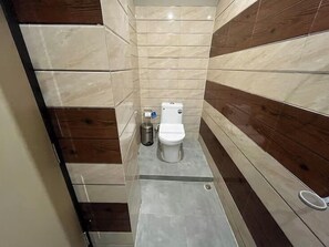 Un baño pequeño y estrecho con inodoro, un basurero y zona de ducha.
