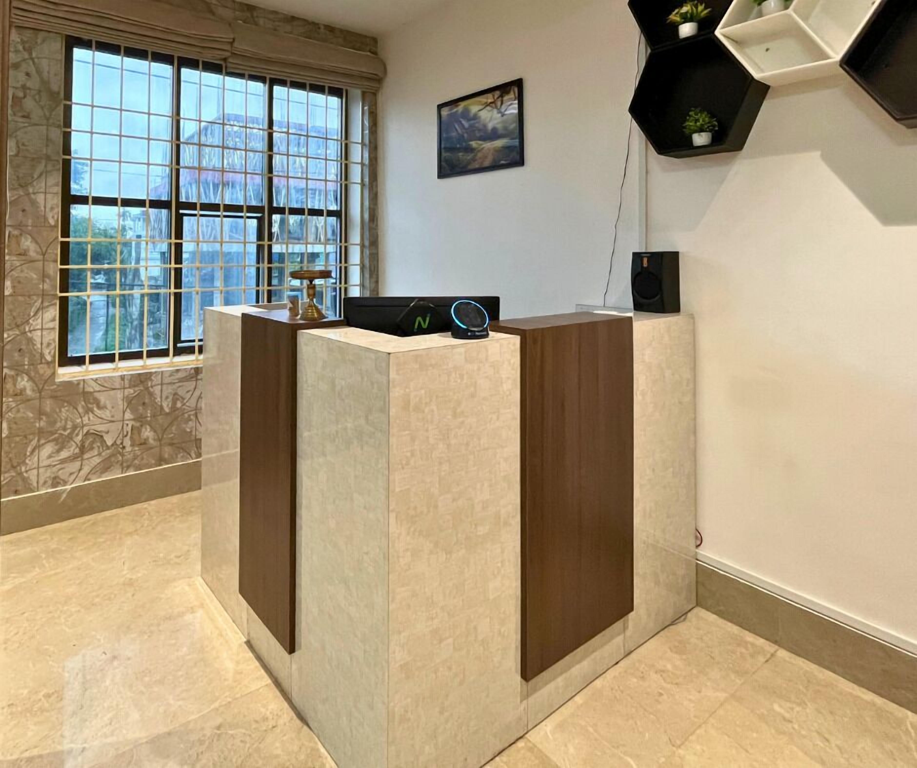 A reception desk with a marble-patterned wall, a window with a view of buildings, and a painting on the wall.