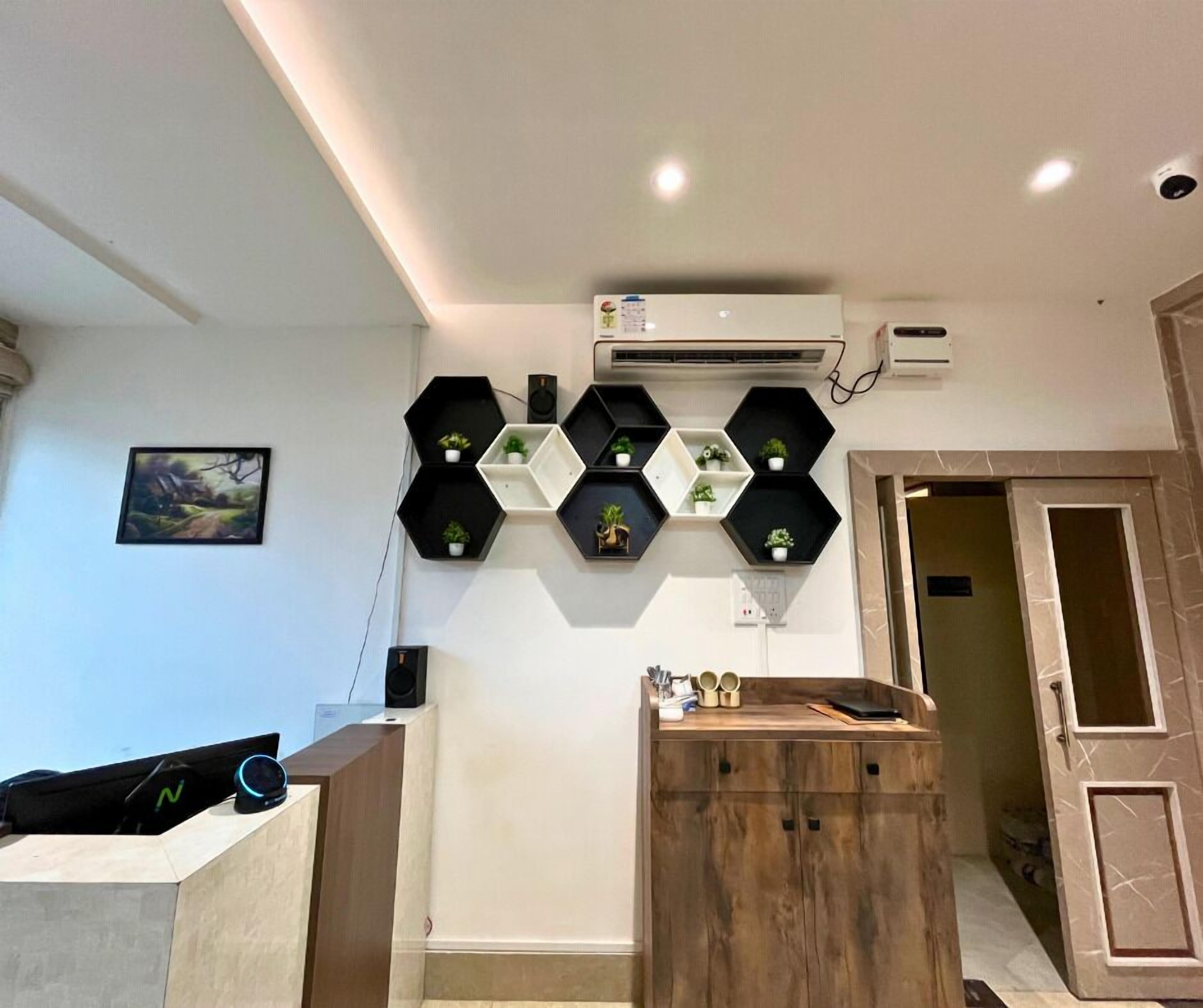 Un interior moderno con un mostrador de recepción de madera, un equipo de aire acondicionado de pared y repisas hexagonales con plantas en macetas.