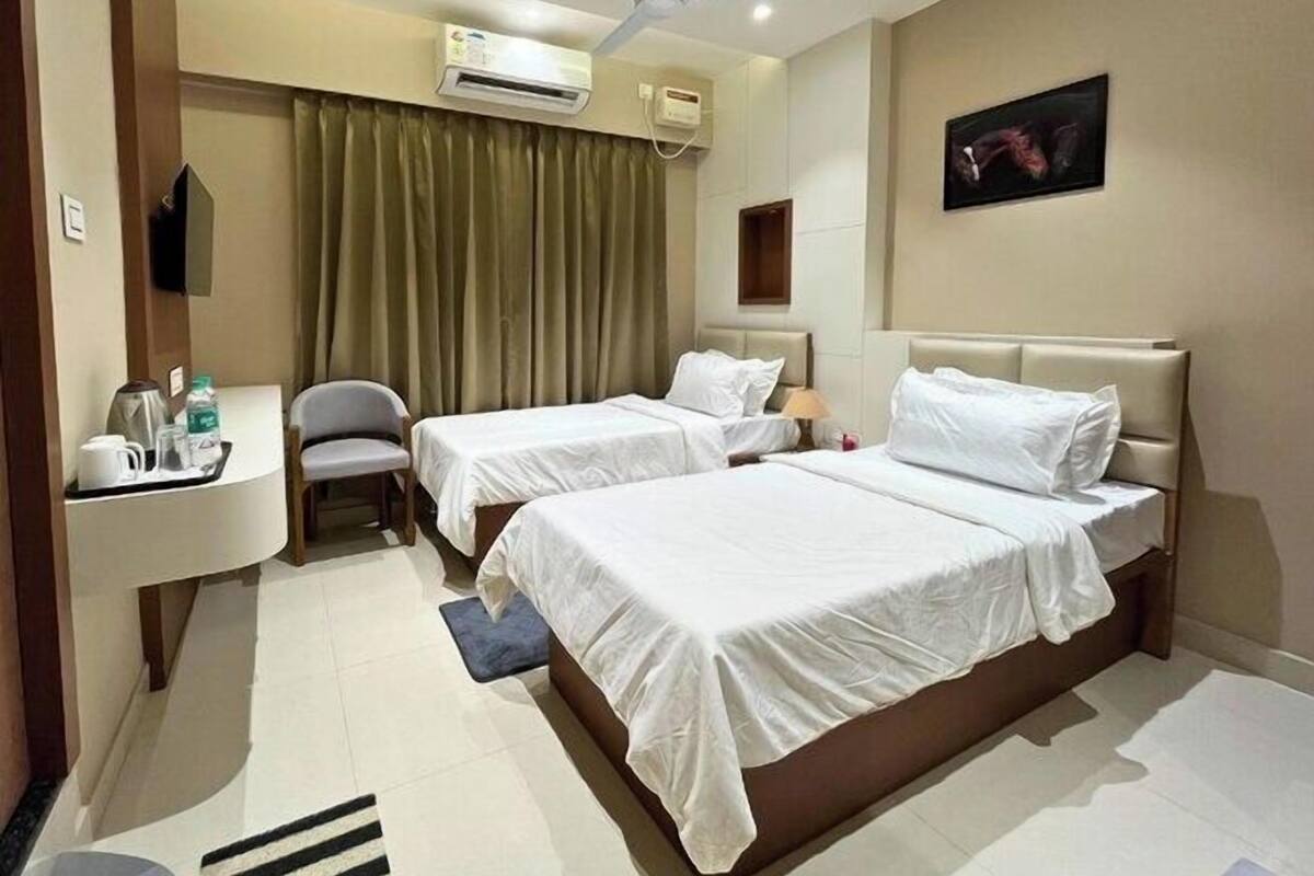 A hotel room with two beds, a desk with a chair, an air conditioning unit, a ceiling fan, and a painting on the wall.
