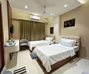 Habitación de hotel con dos camas, un escritorio con silla, aire acondicionado, ventilador de techo y un cuadro en la pared.