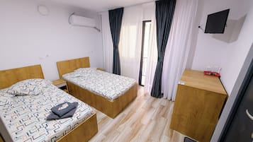 Una habitación de hotel compacta con dos camas individuales, un escritorio de madera, un televisor montado en la pared y una ventana con cortinas.
