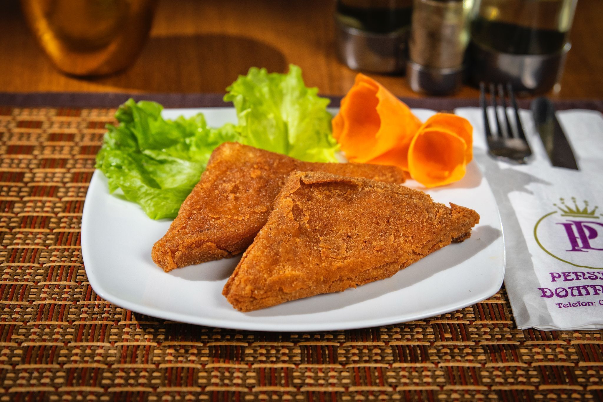 A plate with two triangular fried items, green lettuce, and orange carrot slices on a woven placemat.