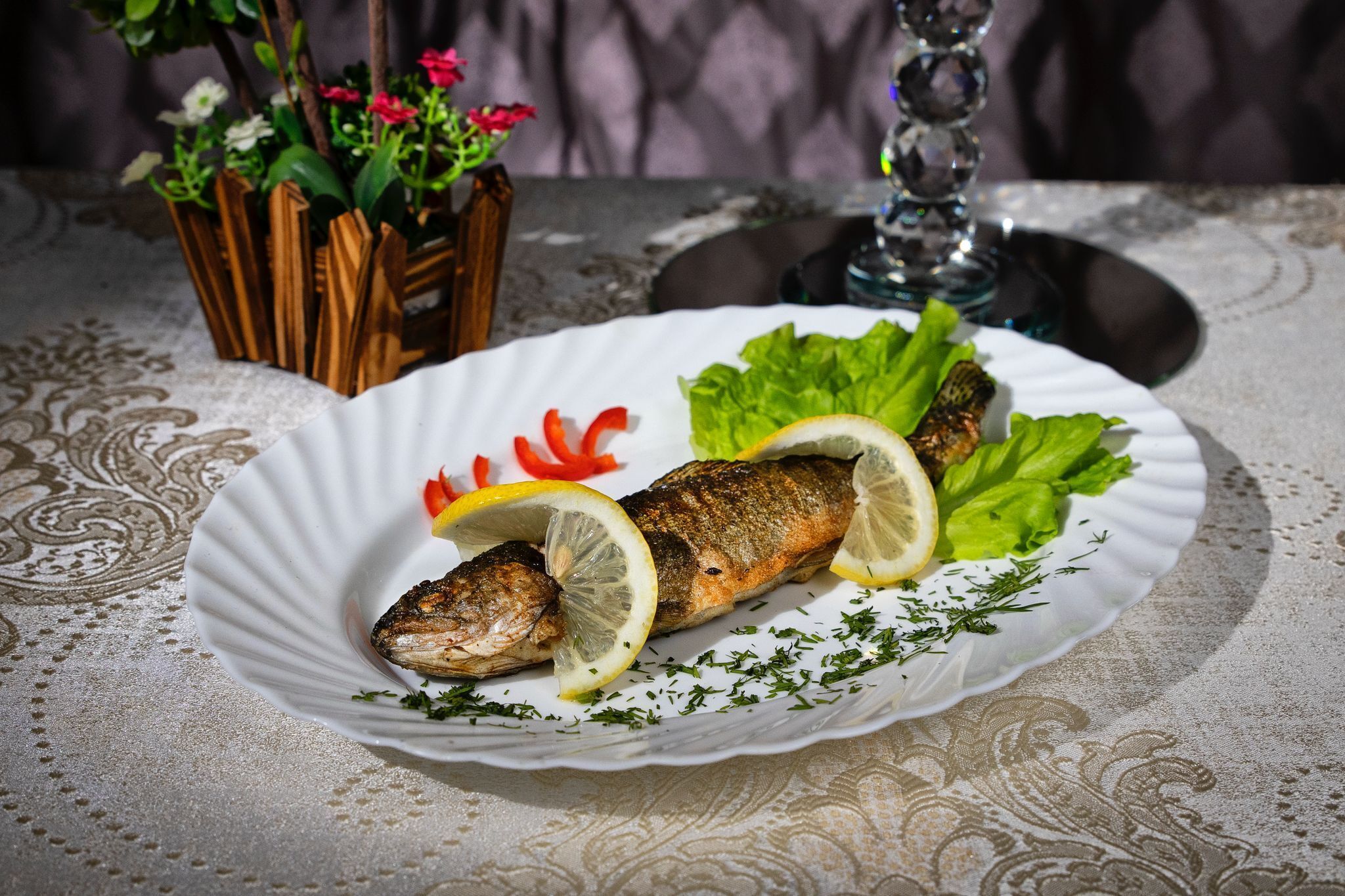 A plate with grilled fish, lemon slices, and lettuce on a tablecloth.