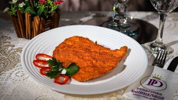 A plate of breaded cutlet with red bell peppers and parsley, a glass of wine, and a napkin with a logo on a tablecloth.