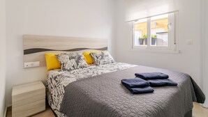 A bedroom with a bed, a nightstand, a window with a view of the outside, and a door. - Holiday Home 'Bungalow Martina for 6 People' with Shared Pool, Wi-Fi and Air Conditioning (Santa Pola)
