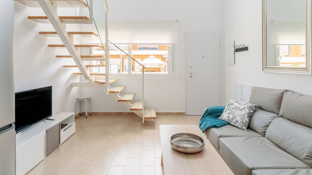A modern living room with a staircase, a flat-screen TV, a sofa, and a large mirror. - Holiday Home 'Bungalow Martina for 6 People' with Shared Pool, Wi-Fi and Air Conditioning (Santa Pola)