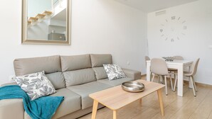 A modern living room with a sofa, a dining table, and a wall clock. - Holiday Home 'Bungalow Martina for 6 People' with Shared Pool, Wi-Fi and Air Conditioning (Santa Pola)