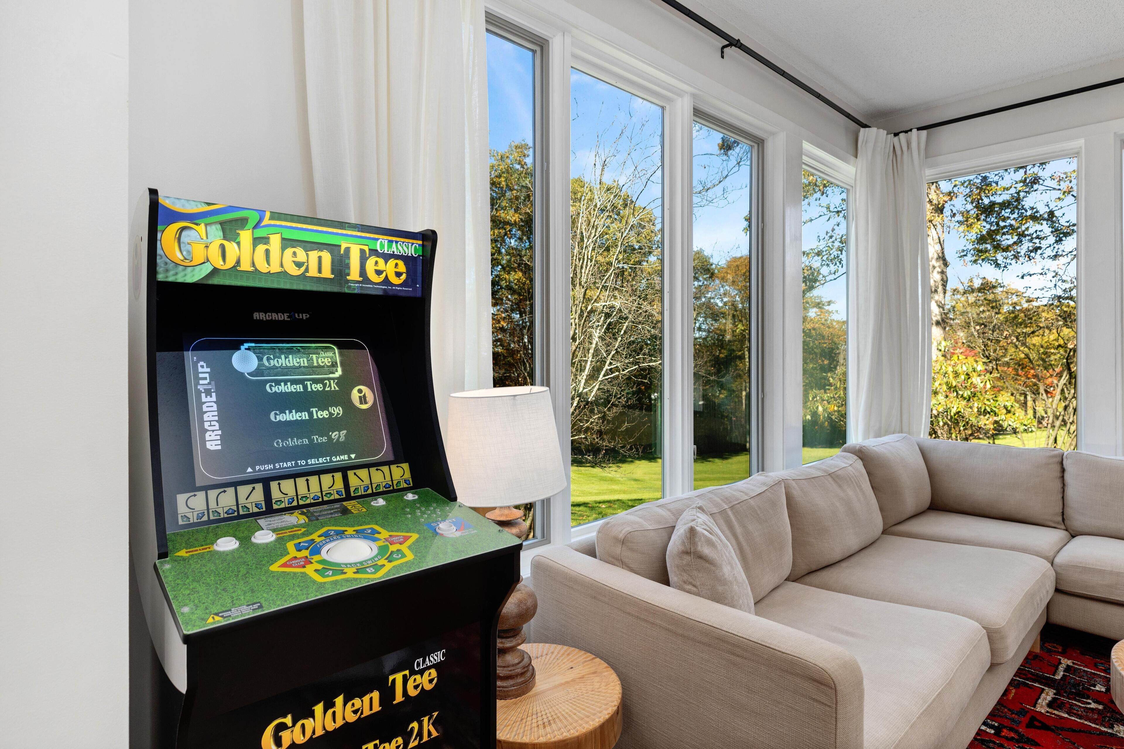 A room with a beige sofa, a table lamp, and a Golden Tee arcade machine.