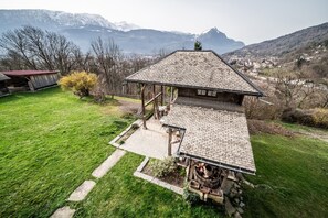 Un chalet rustique doté d’un toit en pente, d’une terrasse en bois et offrant une vue sur des montagnes enneigées.