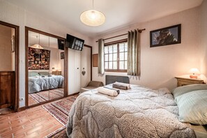 Une chambre à coucher avec un grand lit, une télévision, une fenêtre avec des rideaux, une lampe de chevet et un miroir au mur.