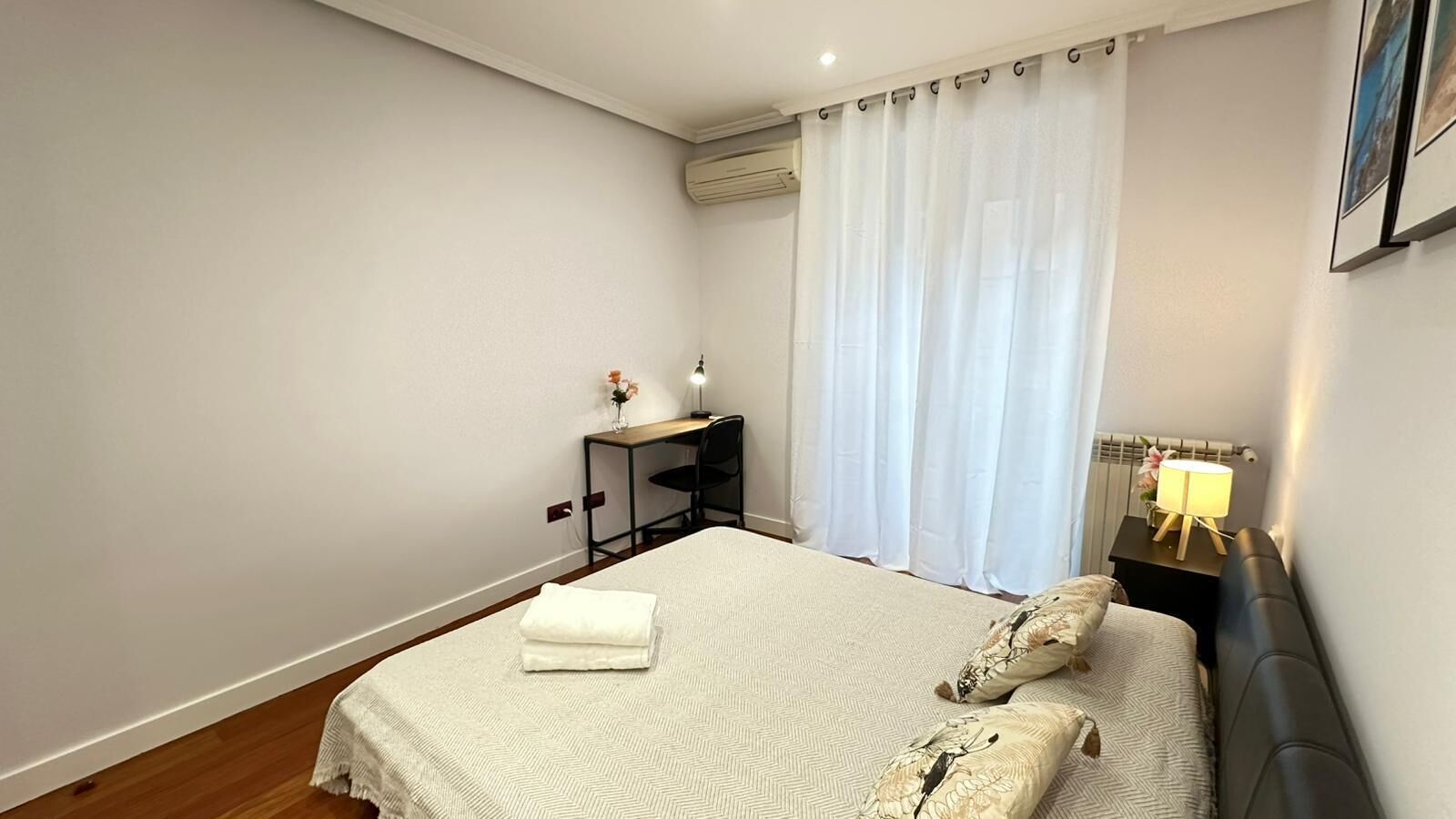 A neatly arranged bedroom with a bed, bedside tables, and a desk.