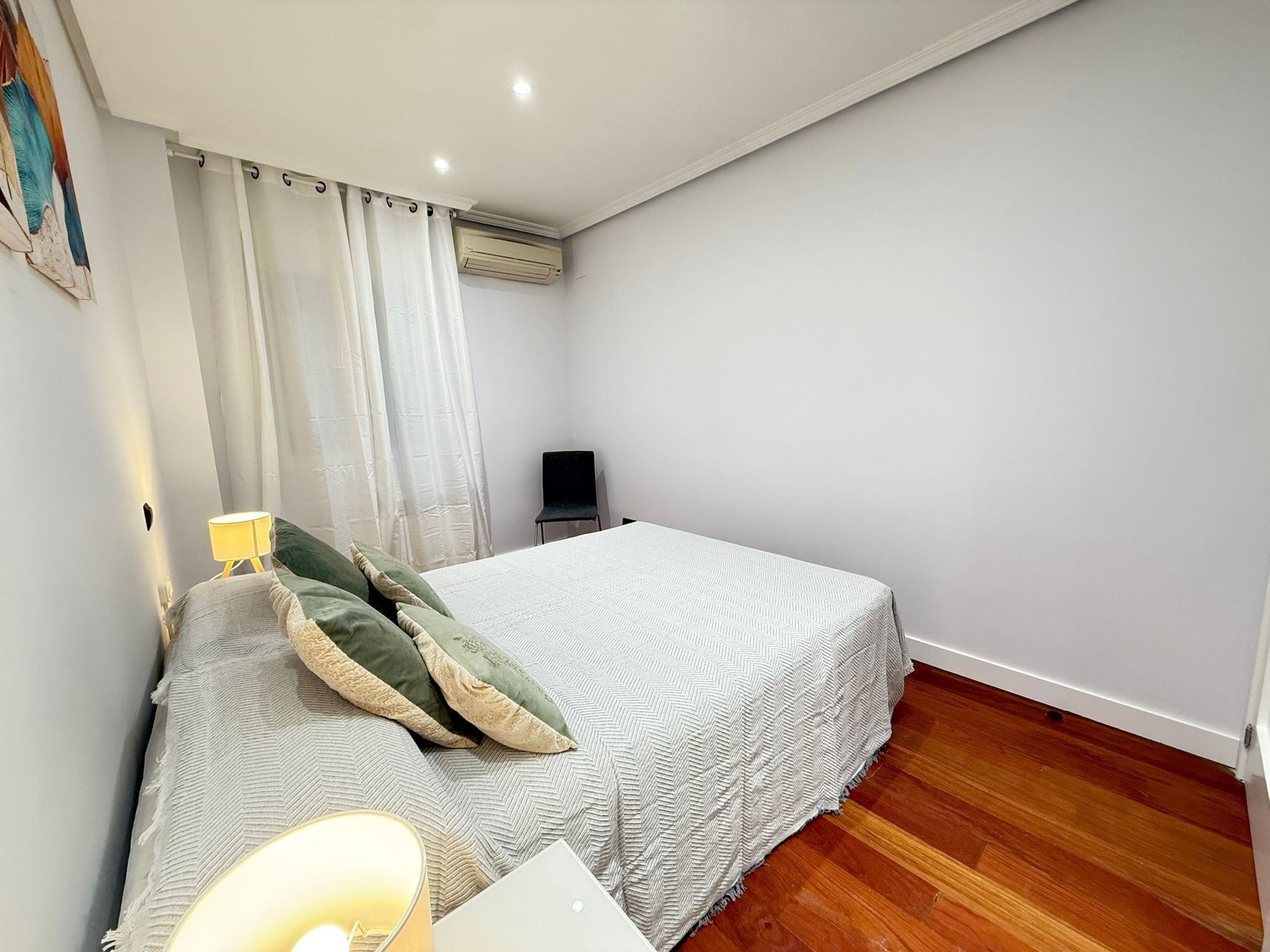 Un dormitorio con una cama, una silla, un escritorio con una computadora portátil y un equipo de aire acondicionado.