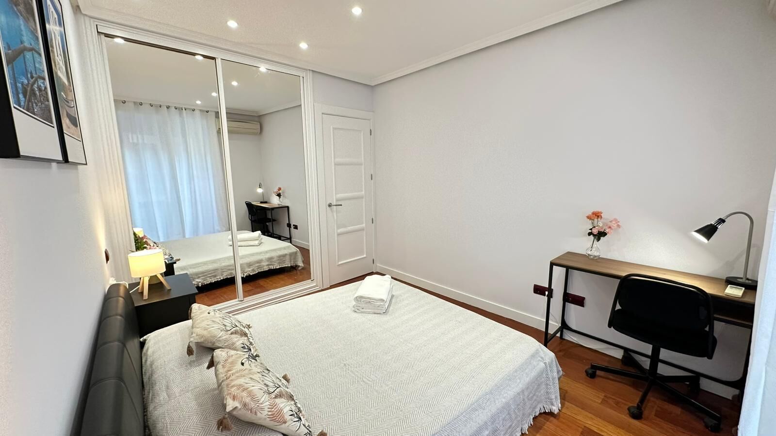 Ein Schlafzimmer mit Bett, Schreibtisch, Stuhl, Spiegel und einem Fenster mit Vorhängen.