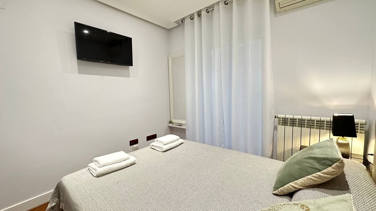 Ein Hotelzimmer mit Bett, Flachbildfernseher an der Wand, Heizkörper und einem Fenster mit Vorhängen.
