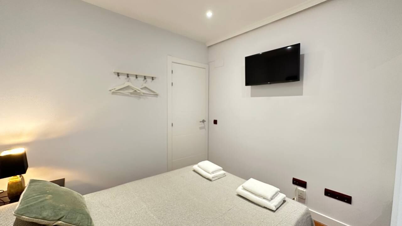 Habitación de hotel con cama, televisor montado en la pared, puerta y perchero.