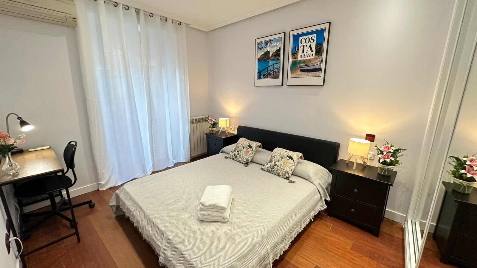 Un dormitorio ordenado con cama, mesitas de noche, escritorio y una silla.
