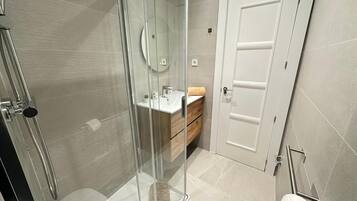 Un baño moderno con cabina de ducha de vidrio, tocador de madera y puerta blanca.