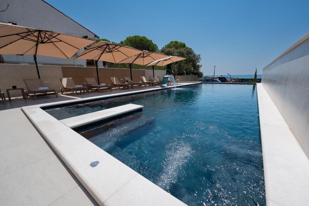En swimmingpool med liggestole og parasoller, et vandfald og udsigt til havet.