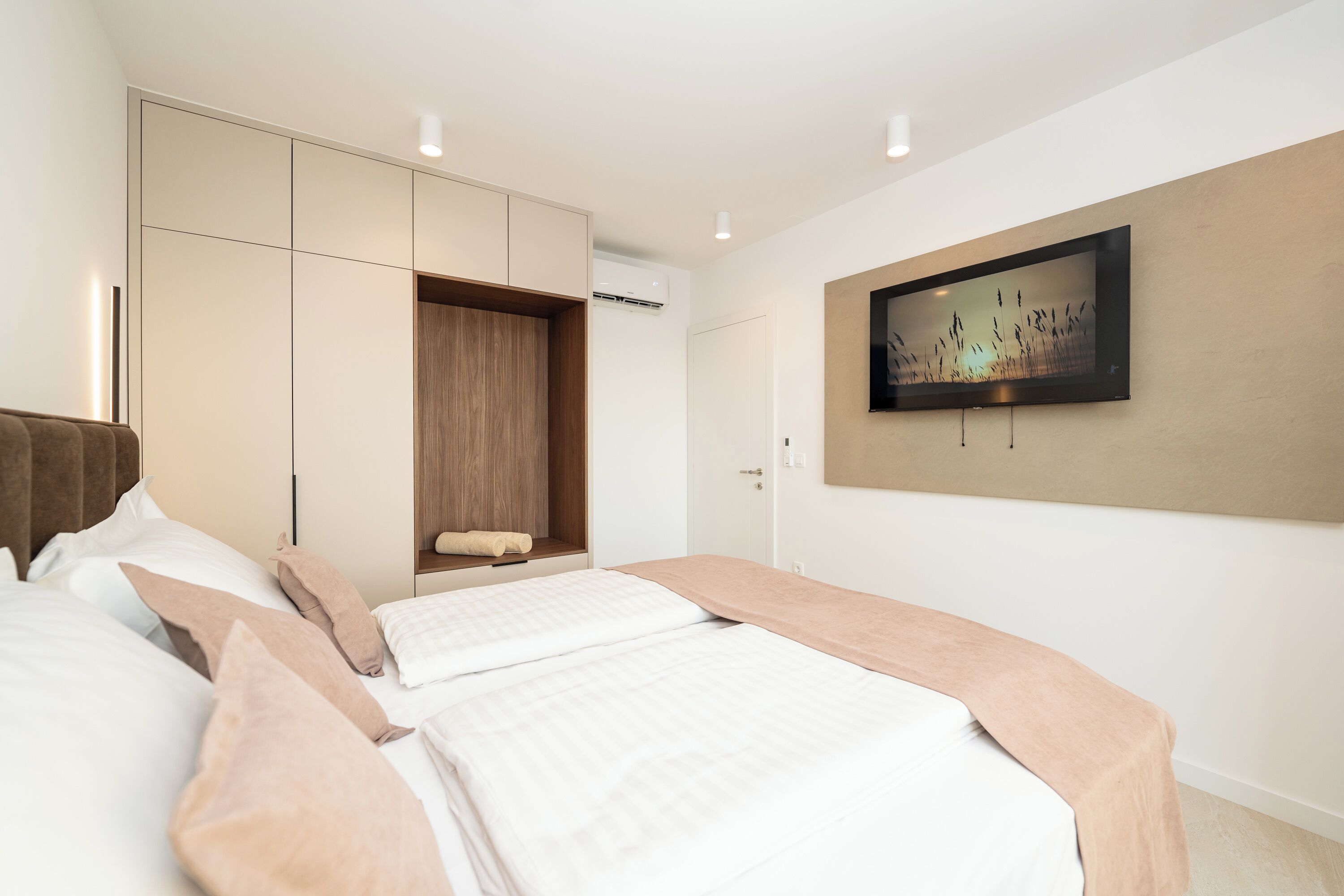 A modern bedroom with a large bed, built-in wardrobe, and a wall-mounted TV.