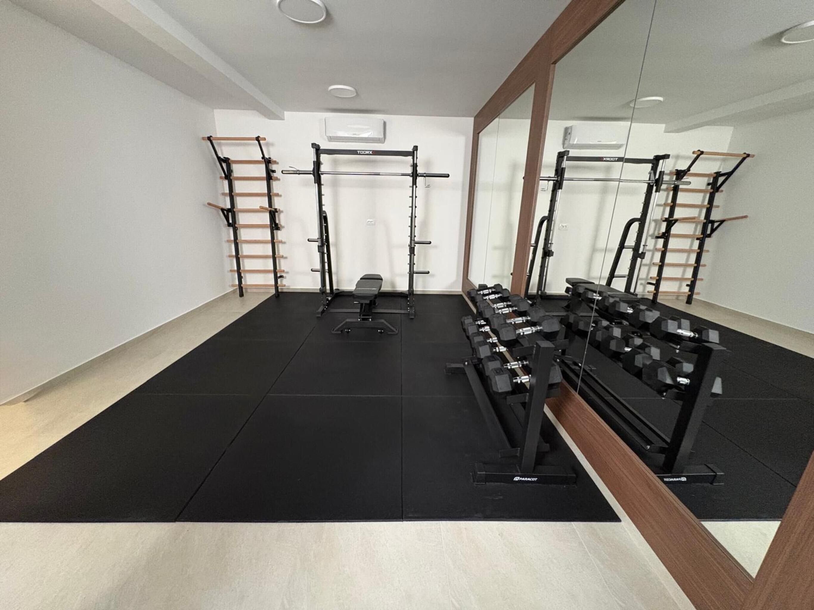 Ein Fitnessraum mit Krafttrainingsgeräten, einer Bank und einem Spiegel.