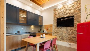 A compact kitchen with a stone wall, a TV mounted above it, and a red refrigerator. - Blu's house in Florence (Firenze)