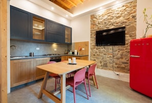 A compact kitchen with a stone wall, a TV mounted above it, and a red refrigerator.