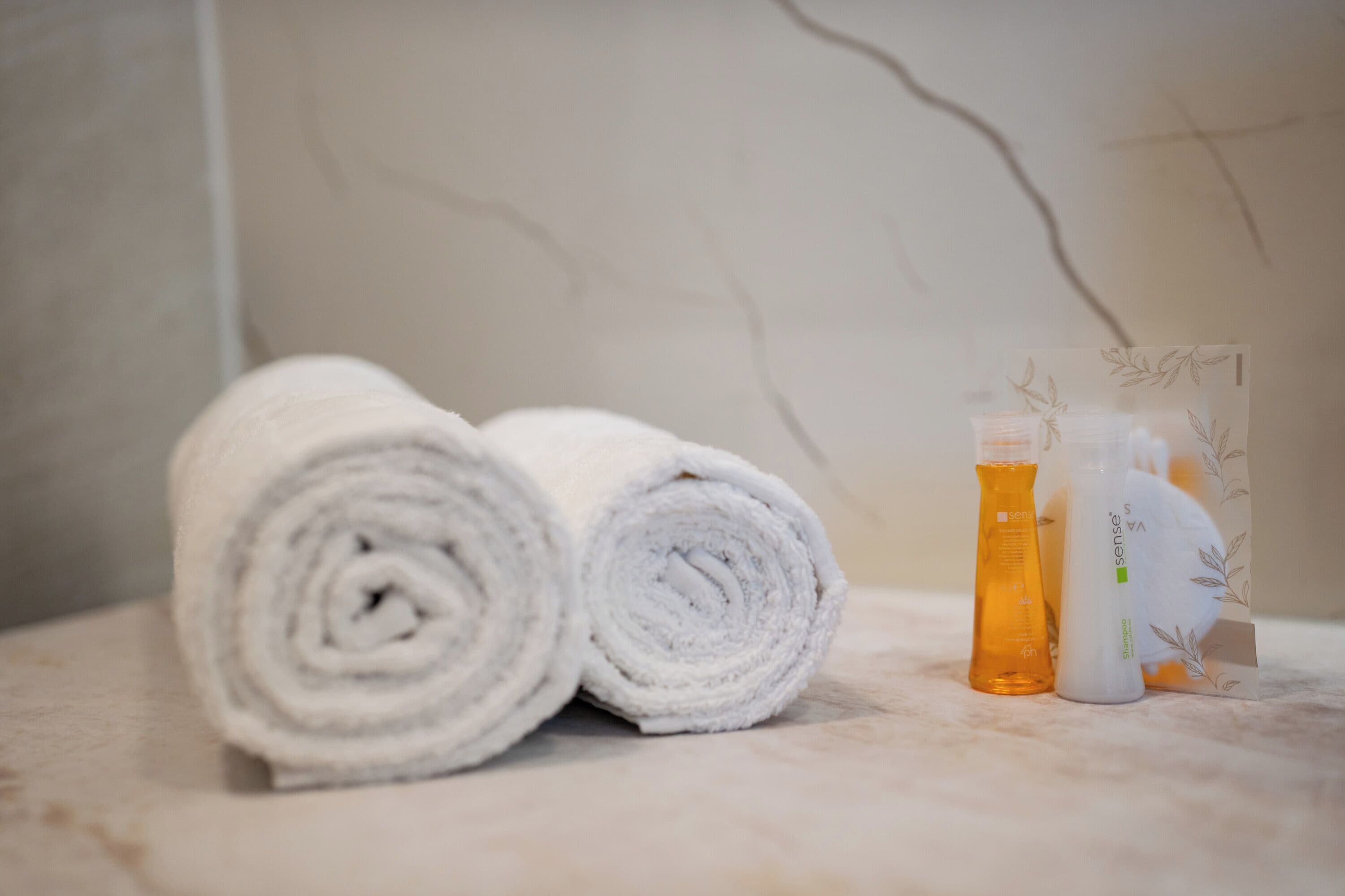 Two rolled white towels and two bottles of shampoo on a marble surface.