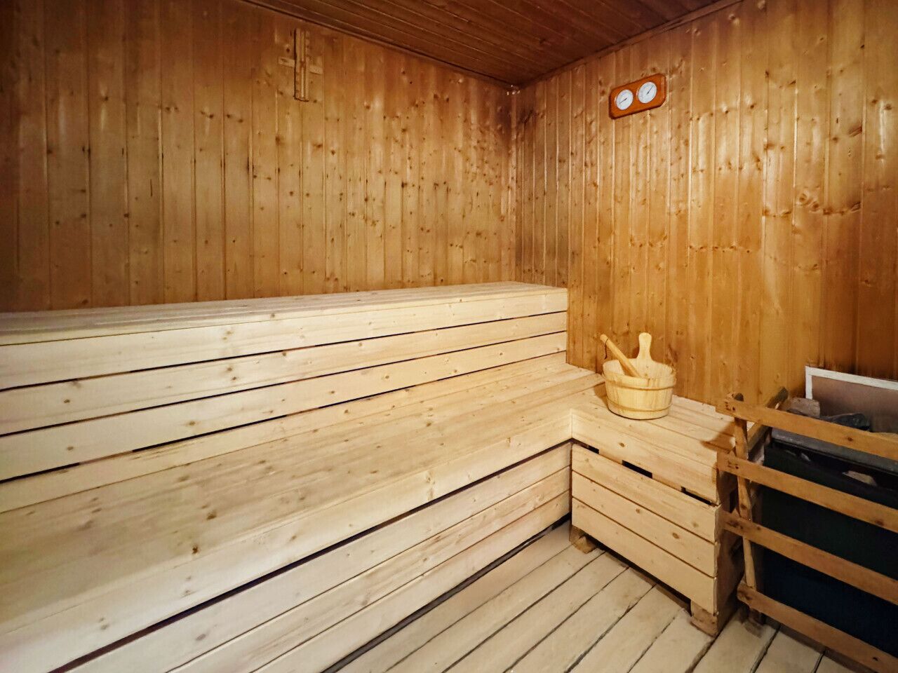Una sauna in legno con panche, un catino di legno e una sveglia al muro.