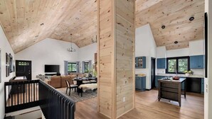 A spacious living area with a high ceiling, wooden flooring, and a modern kitchen with blue cabinets. - Cedar Hill Lodge | 10 Min to Mt Snow w/Hot Tub (Wardsboro)